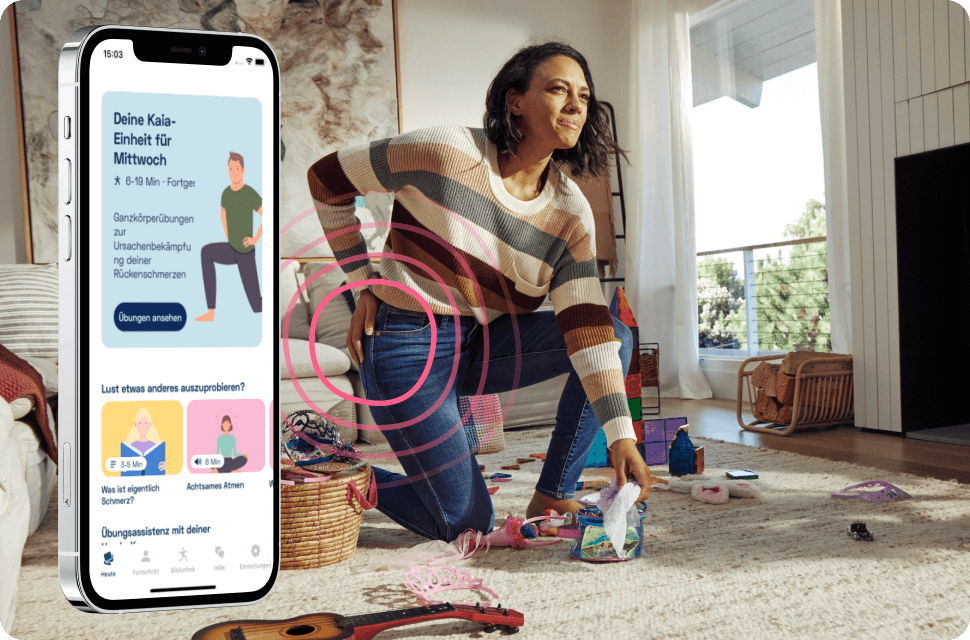 Mobiltelefon mit Kaia Rückenschmerz App vor Frau, die sich schmerzerfüllt den Rücken reibt, während sie Spielzeug vom Boden einsammelt