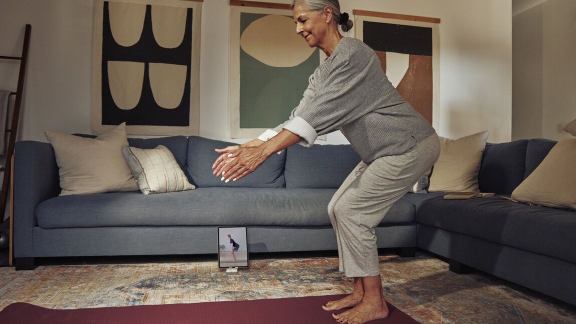 Ältere Frau macht Rückenübungen mit Tablet