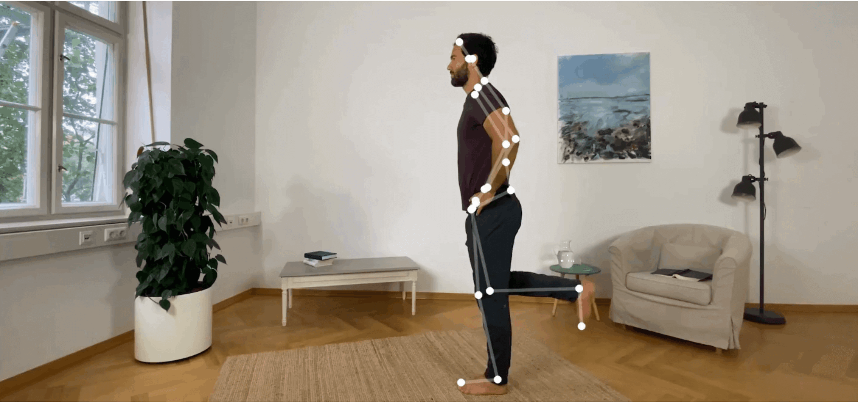 Ein junger Mann führt eine stehende Übung aus, bei der er auf dem linken Bein steht und seinen rechten Unterschenkel hebt. Auf seinem Körper sind digitale Marker sichtbar, die den Algorithmus des Bewegungscoaches dabei unterstützen, die Lage des Körpers in Raum zu erkennen.